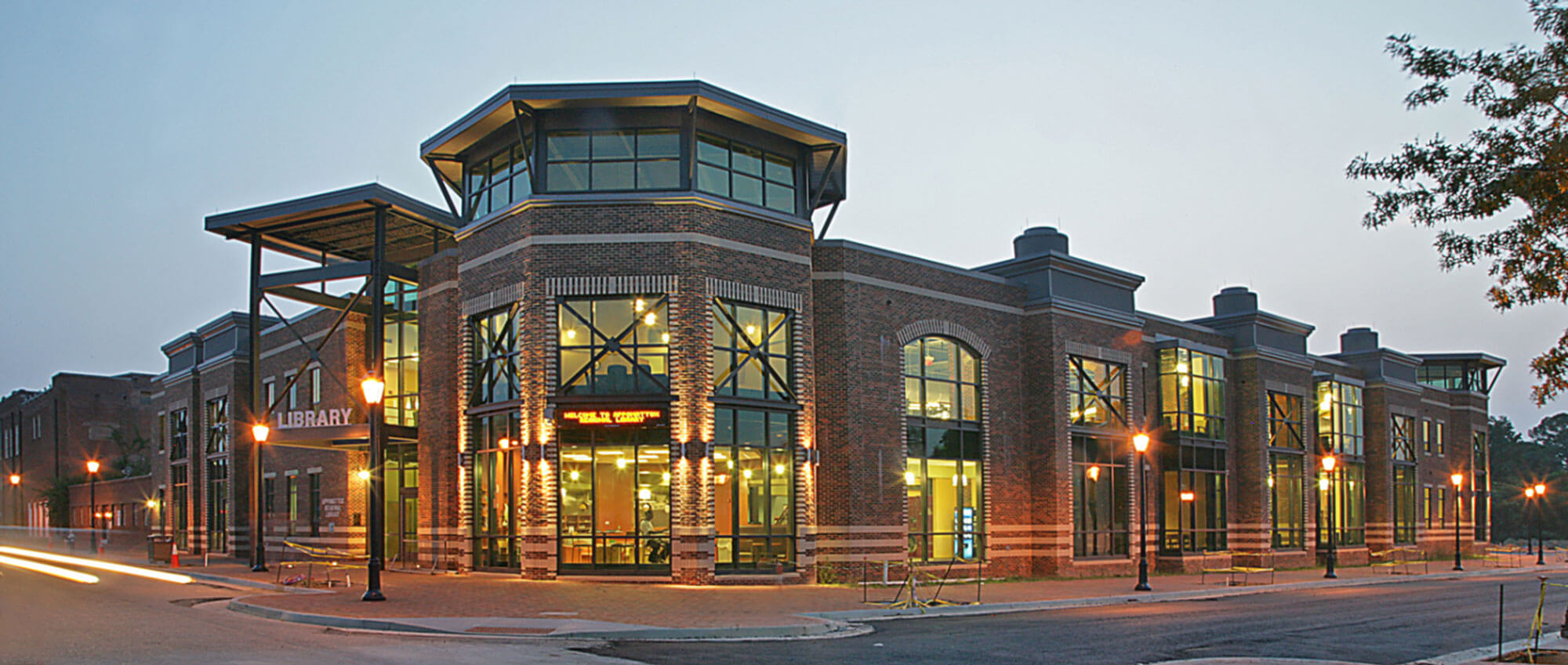 Brick library building at dusk with large glass windows and warm exterior lighting.